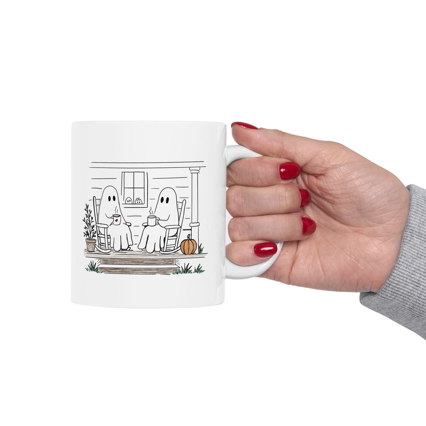 White ceramic mug featuring a hand-drawn ghost family sitting on a front porch in rocking chairs with coffee, with two little ghosts peeking through the window and subtle fall color accents.