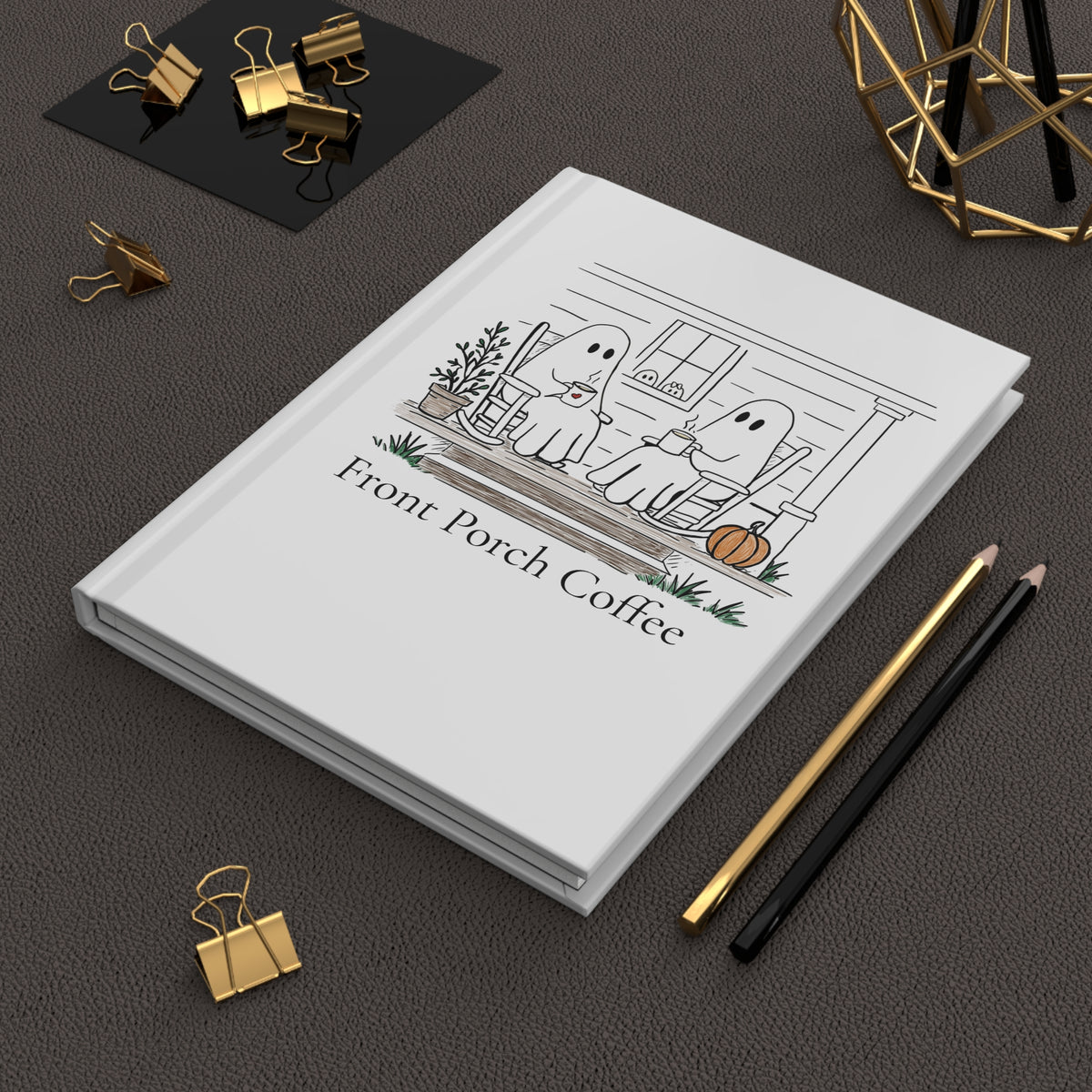 White notebook with a design on the cover, placed on a dark surface with office supplies.