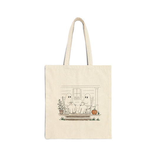 Natural canvas tote bag featuring a hand-drawn ghost family relaxing with coffee in rocking chairs on a front porch, with two little ghosts peeking through the window, a pumpkin, and subtle fall accents.