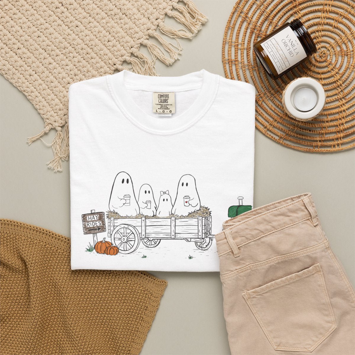 Comfort Colors white t-shirt featuring a hand-drawn ghost family riding in a hay wagon with pumpkins, coffee mugs, and a vintage tractor from The Story of the Ghost Chapter 1 collection.