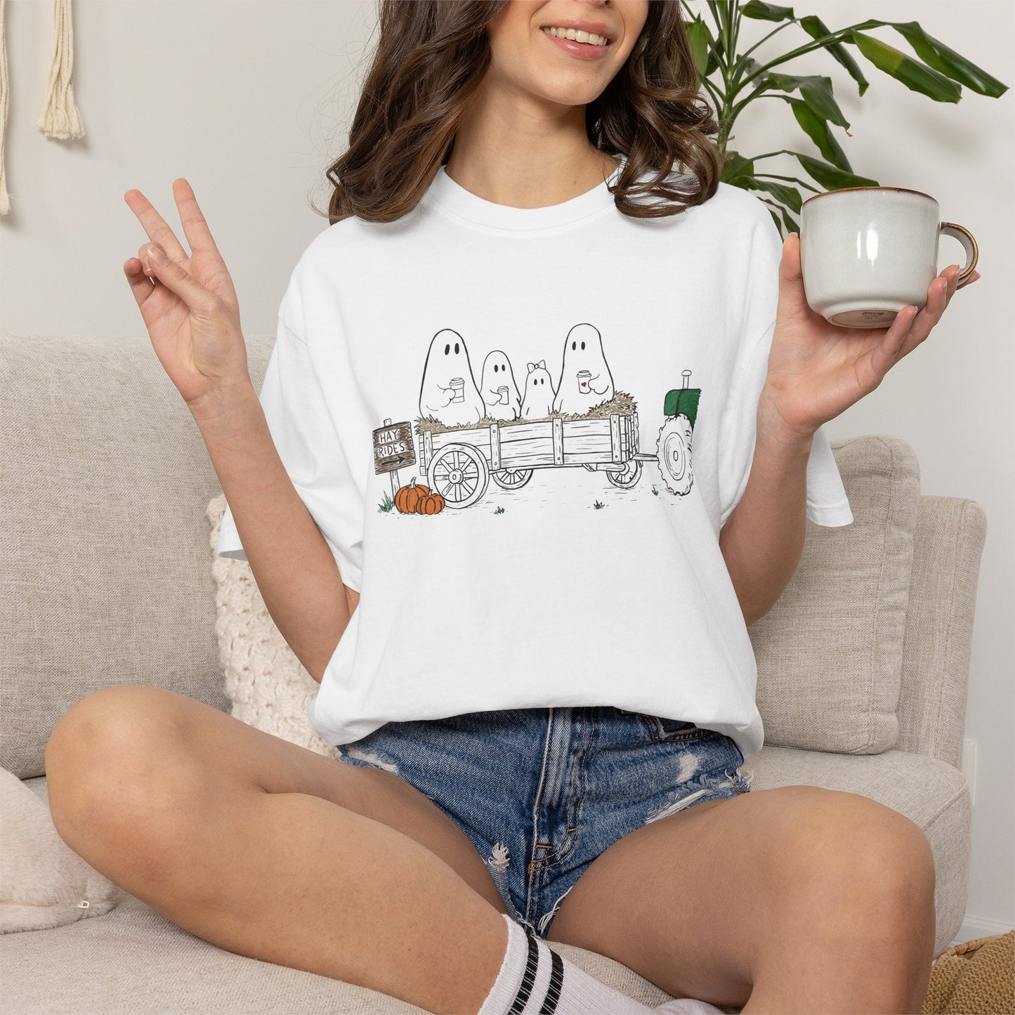 Comfort Colors white t-shirt featuring a hand-drawn ghost family riding in a hay wagon with pumpkins, coffee mugs, and a vintage tractor from The Story of the Ghost Chapter 1 collection.