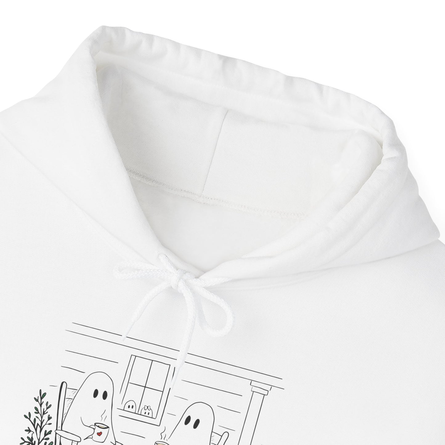 Close-up of a white hoodie showing the hood lining, drawstring, and a partial black line-art graphic of ghosts in front of a house.