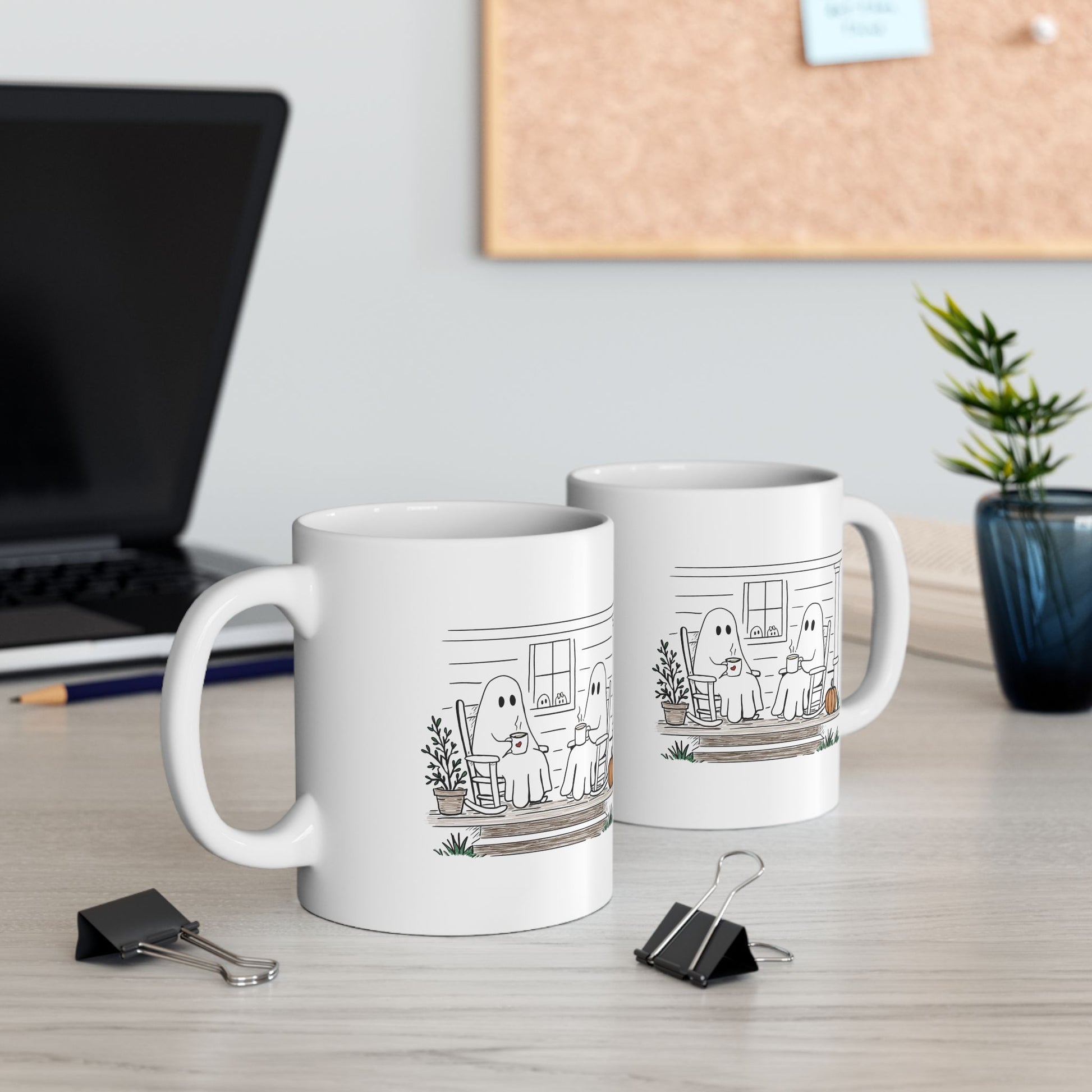 White ceramic mug featuring a hand-drawn ghost family sitting on a front porch in rocking chairs with coffee, with two little ghosts peeking through the window and subtle fall color accents.