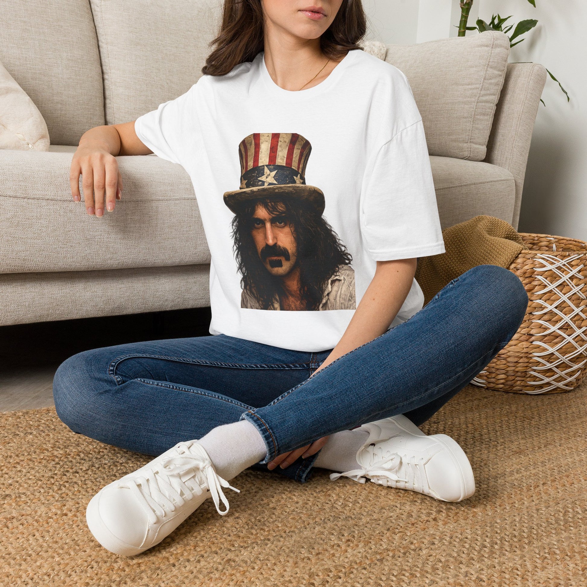 Person wearing a white t-shirt with a graphic design of a person wearing an American flag hat, sitting on a carpeted floor.