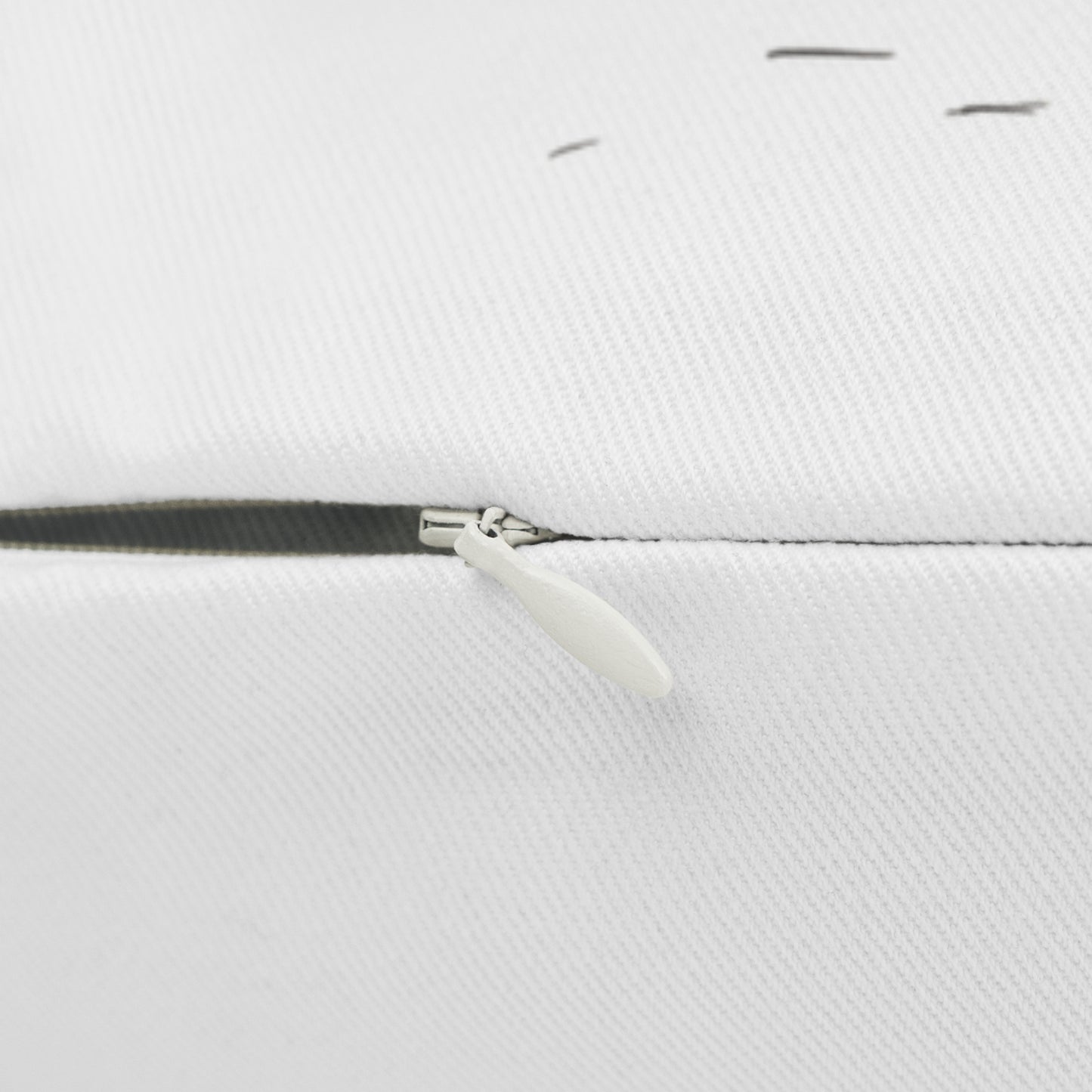 Close-up of a white woven fabric surface with a black zipper track and a small white pull tab.