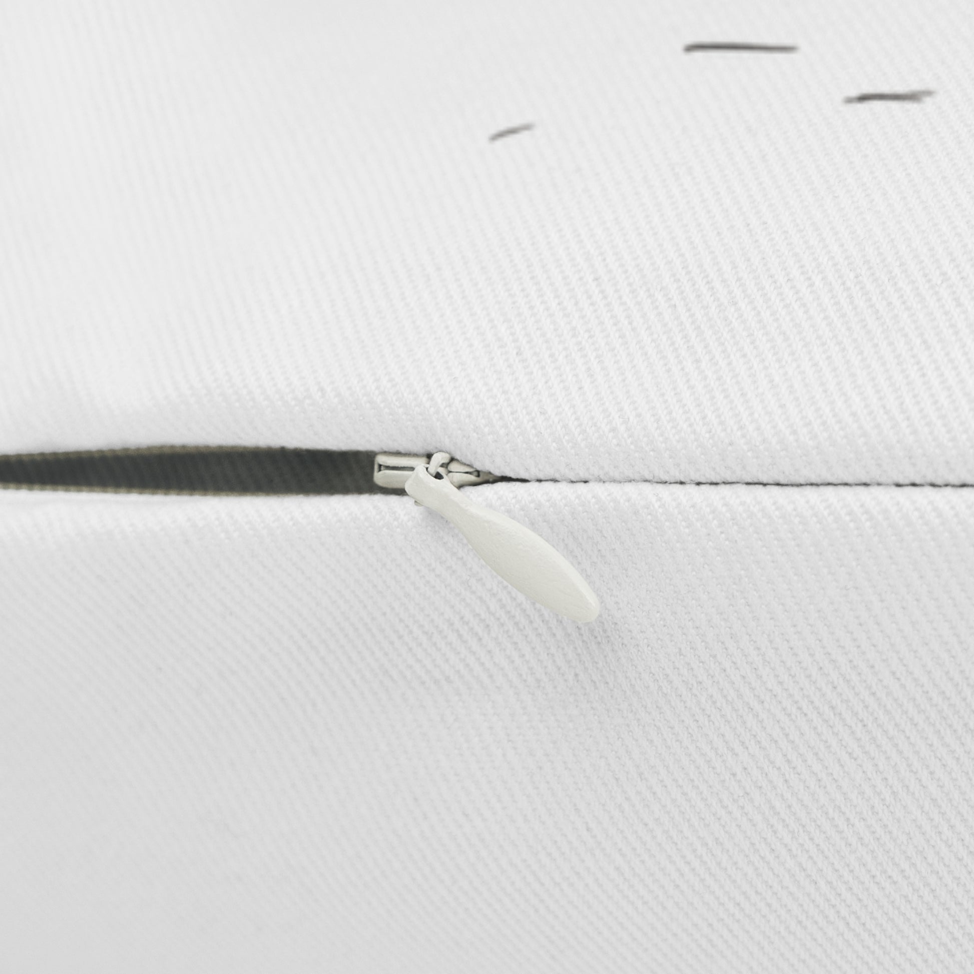 Close-up of a white woven fabric surface with a black zipper track and a small white pull tab.