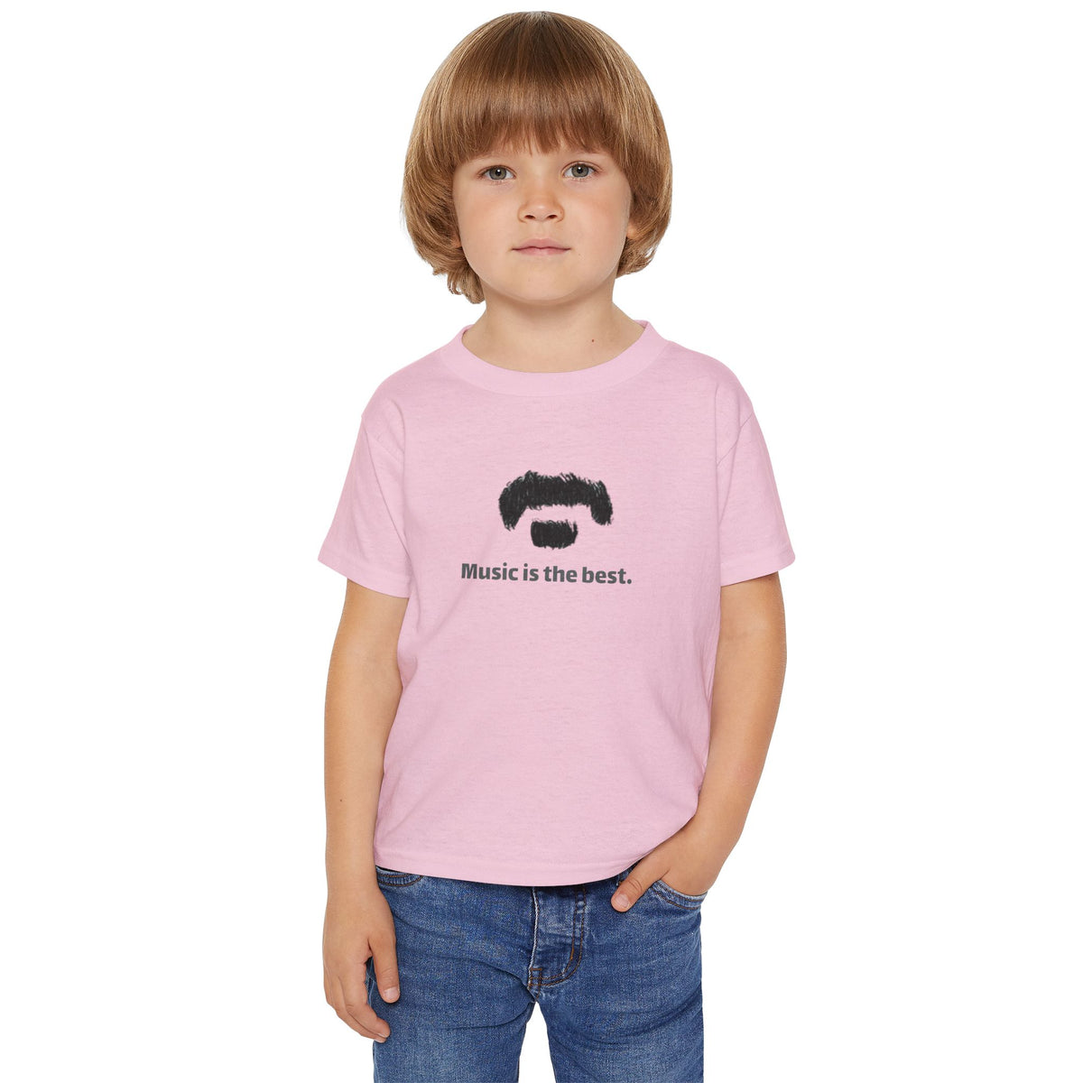 A young boy with light brown hair wearing a light pink t-shirt with the text 'music is the best' in black, paired with blue jeans, standing against a plain white background.