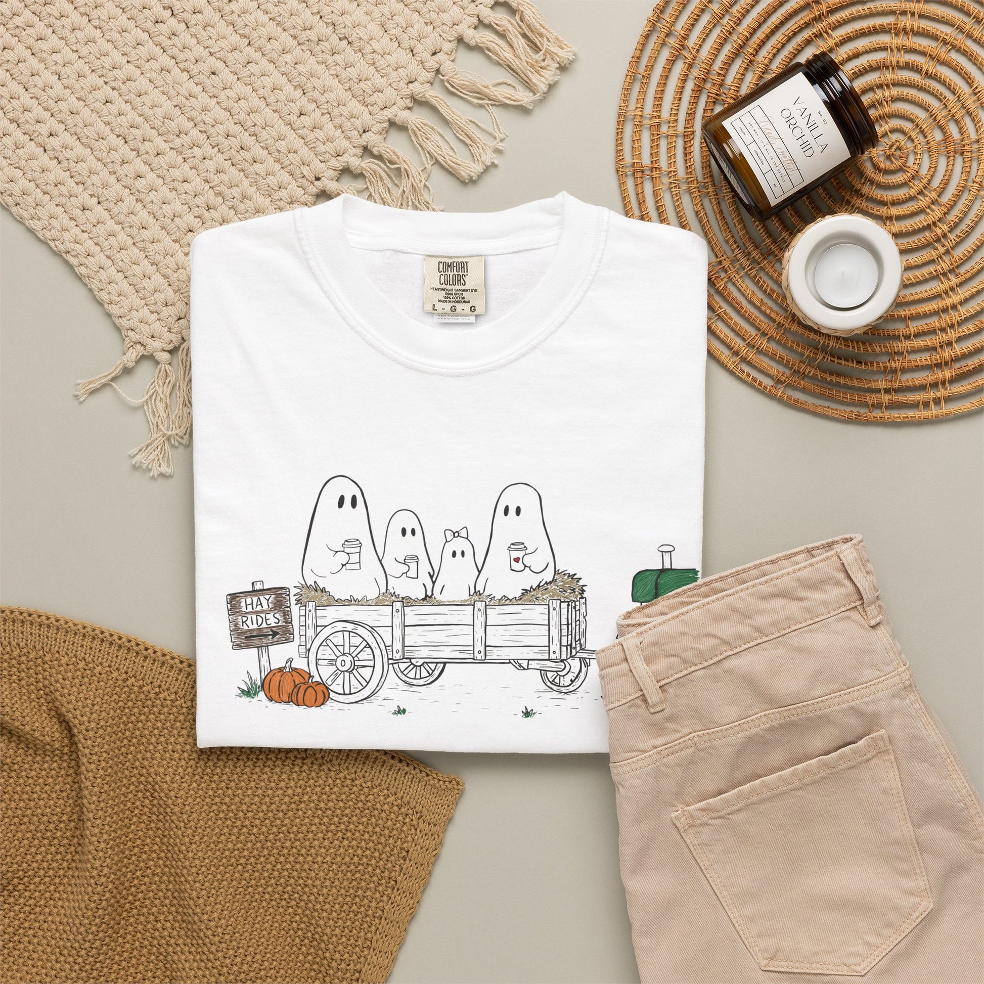 Comfort Colors white t-shirt featuring a hand-drawn ghost family riding in a hay wagon with pumpkins, coffee mugs, and a vintage tractor from The Story of the Ghost Chapter 1 collection.