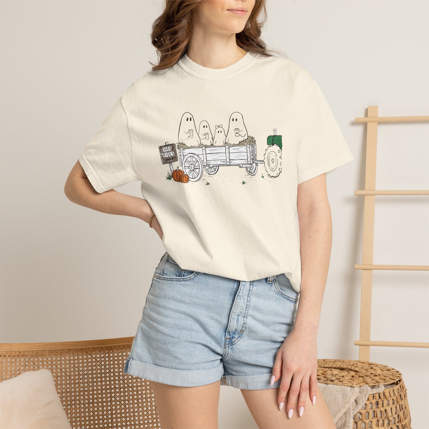 Comfort Colors ivory t-shirt featuring a hand-drawn ghost family riding in a hay wagon with pumpkins, coffee mugs, and a vintage tractor from The Story of the Ghost Chapter 1 collection.