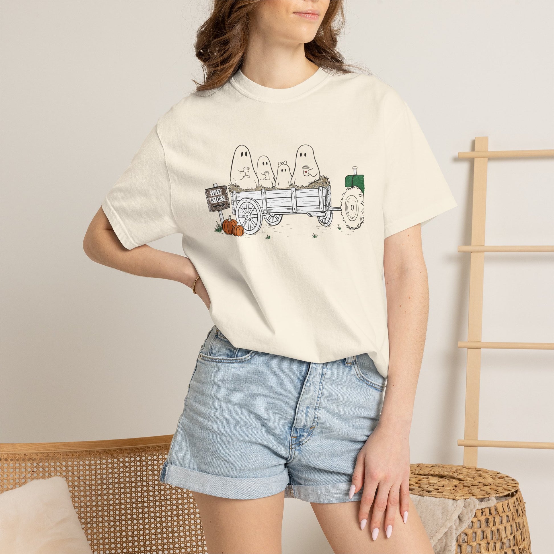 Comfort Colors ivory t-shirt featuring a hand-drawn ghost family riding in a hay wagon with pumpkins, coffee mugs, and a vintage tractor from The Story of the Ghost Chapter 1 collection.