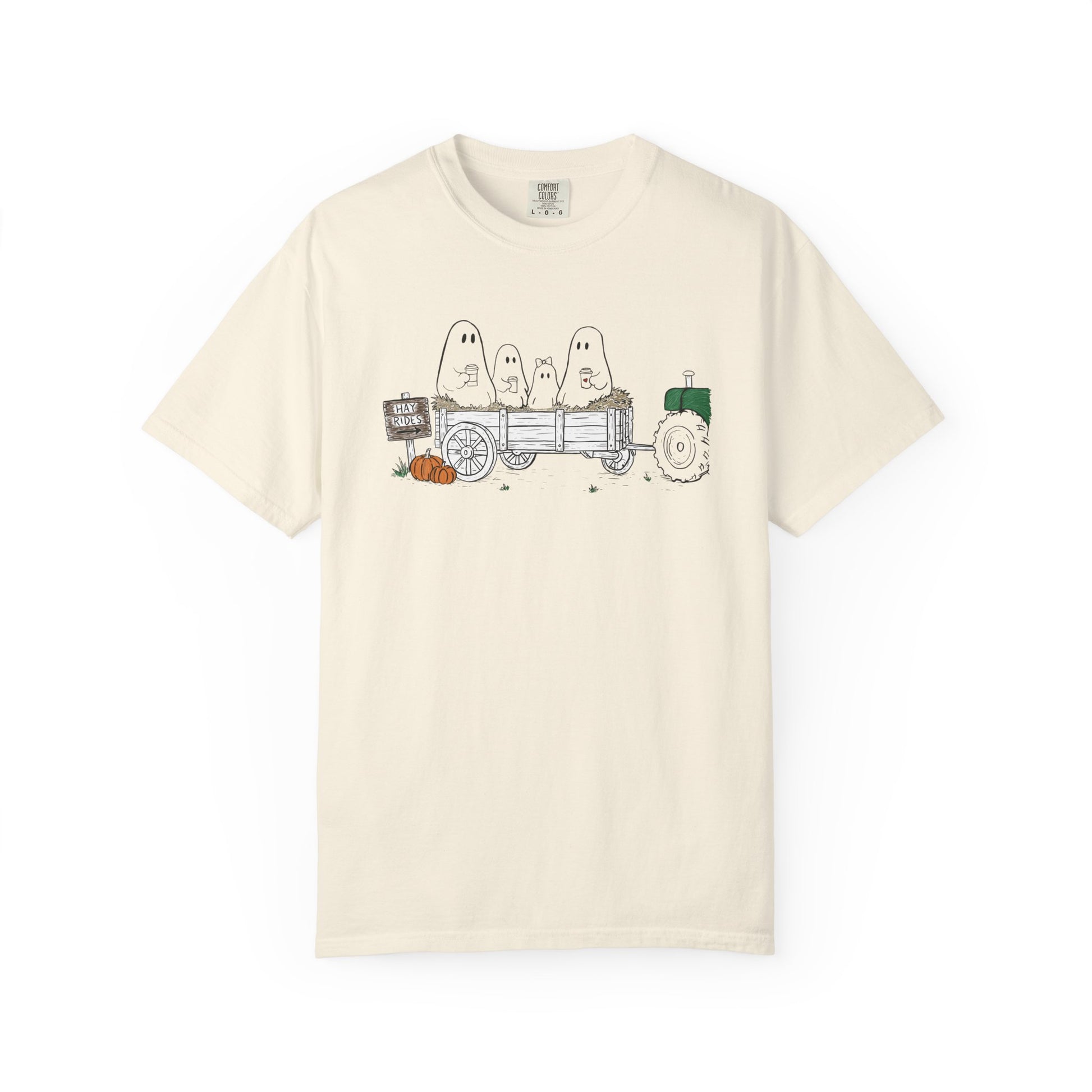 Comfort Colors ivory t-shirt featuring a hand-drawn ghost family riding in a hay wagon with pumpkins, coffee mugs, and a vintage tractor from The Story of the Ghost Chapter 1 collection.