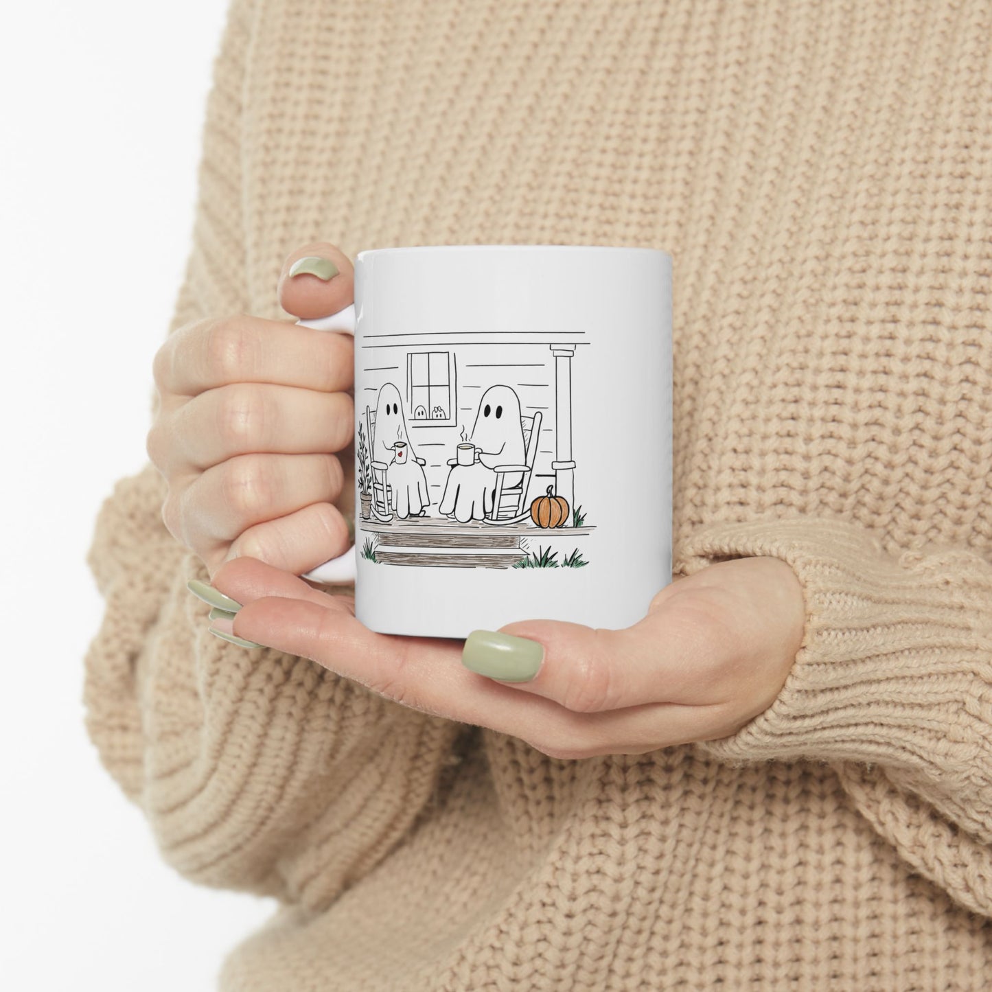 White ceramic mug featuring a hand-drawn ghost family sitting on a front porch in rocking chairs with coffee, with two little ghosts peeking through the window and subtle fall color accents.