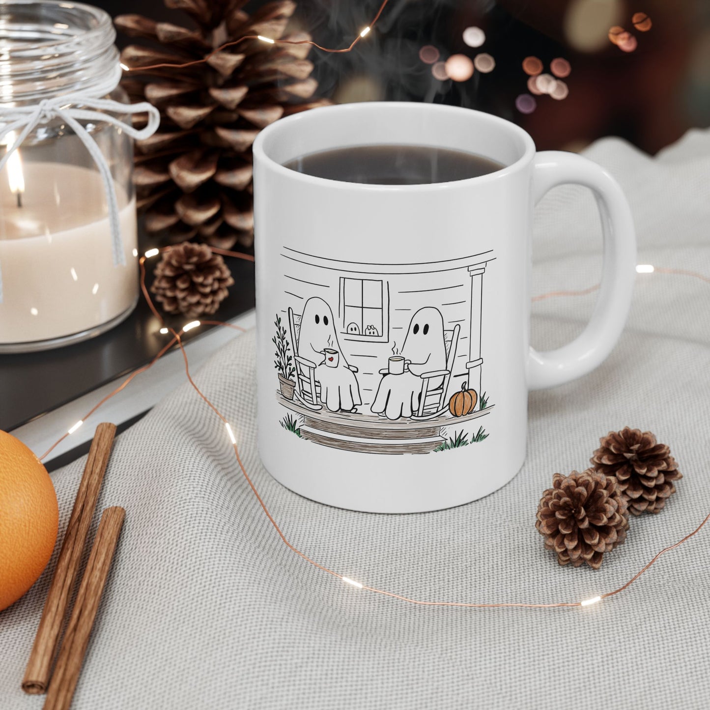 White ceramic mug featuring a hand-drawn ghost family sitting on a front porch in rocking chairs with coffee, with two little ghosts peeking through the window and subtle fall color accents.