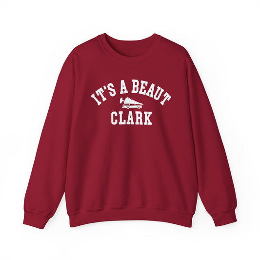 A maroon crewneck sweatshirt with 'IT'S A BEAUT CLARK' printed in white arched text across the chest, featuring a small white wagon with a Christmas tree graphic in the center.