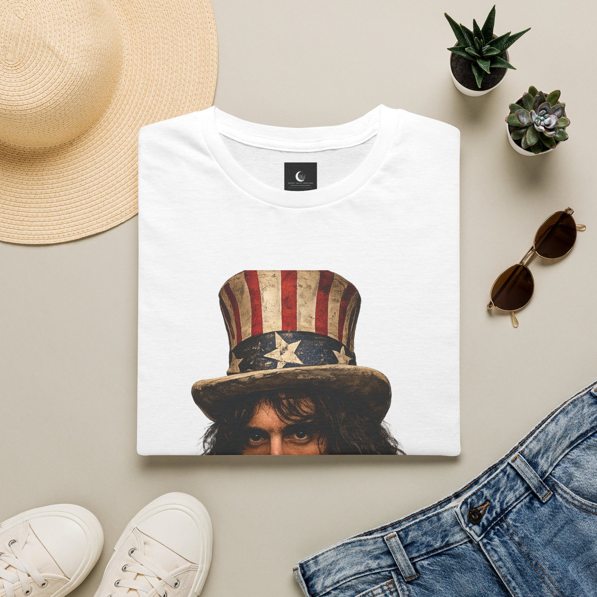White t-shirt with graphic design of a person wearing an American flag hat, surrounded by a straw hat, sunglasses, sneakers, and plants on a beige surface.