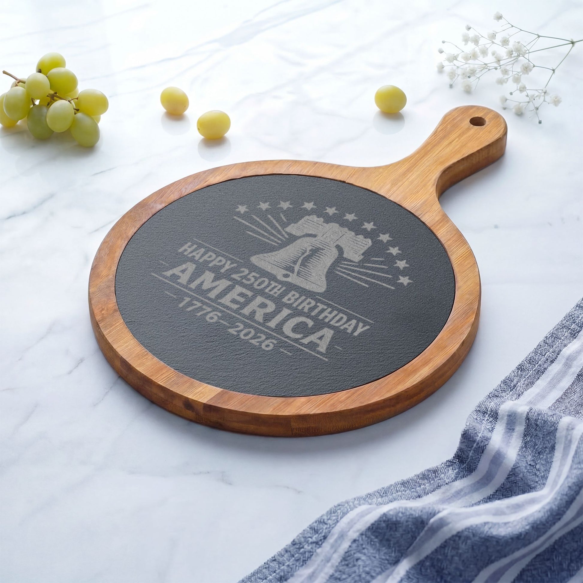 Round wooden cutting board with engraved text on a white surface with grapes and a towel.