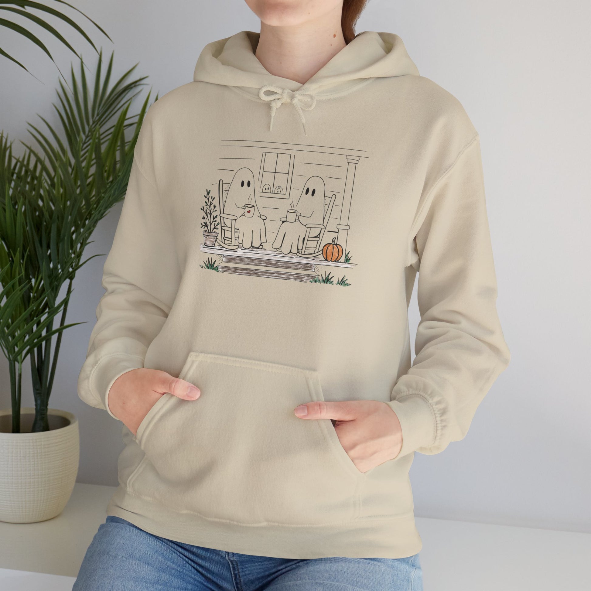 Pullover hoodie featuring a hand-drawn ghost family enjoying coffee in rocking chairs on a front porch, with two little ghosts peeking through the window, a pumpkin, and subtle fall color accents.