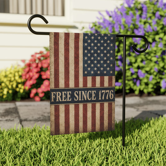 American flag garden flag with 'Free Since 1776' text on grass with flowers in the background