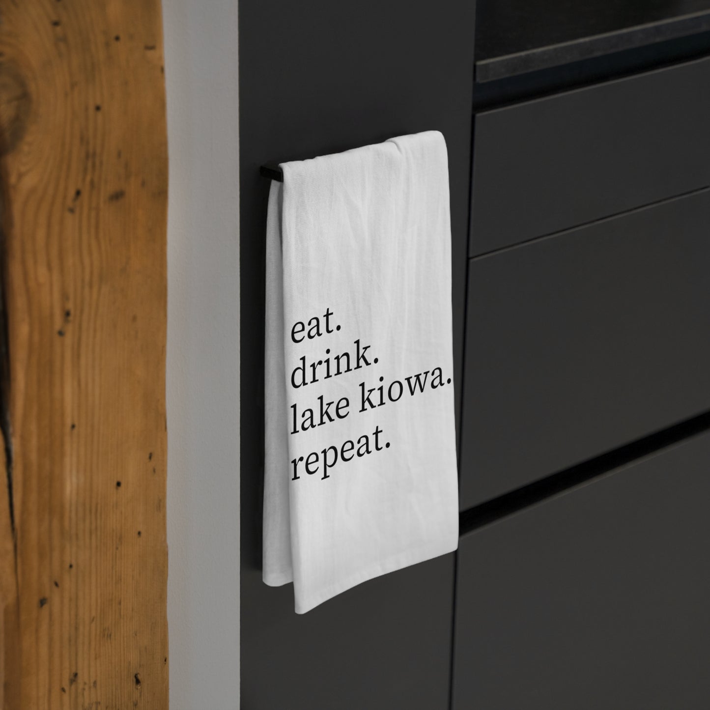 White towel with black text and design hanging on a black cabinet.