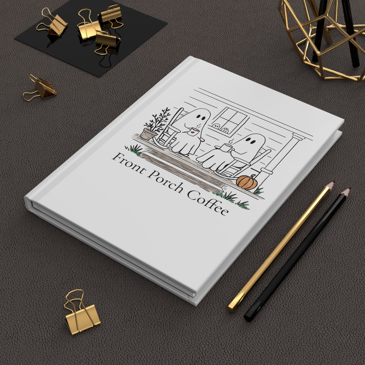 White notebook with a design on the cover, placed on a dark surface with office supplies.