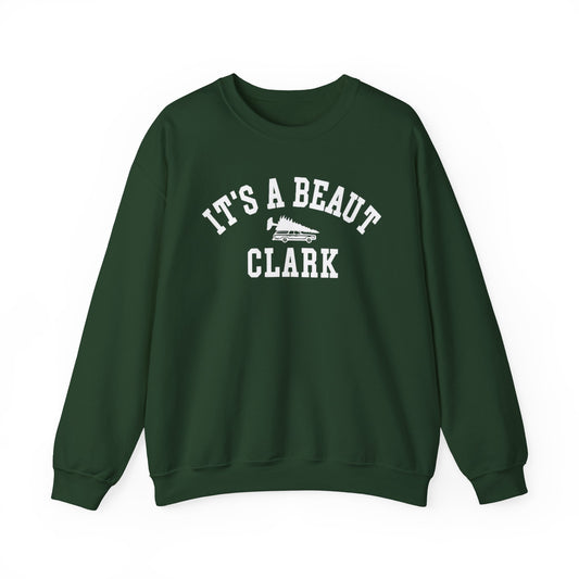 A dark green crewneck sweatshirt with a white graphic print on the front that reads 'IT'S A BEAUT CLARK' with a small wagon and Christmas tree, displayed on a clean white background.