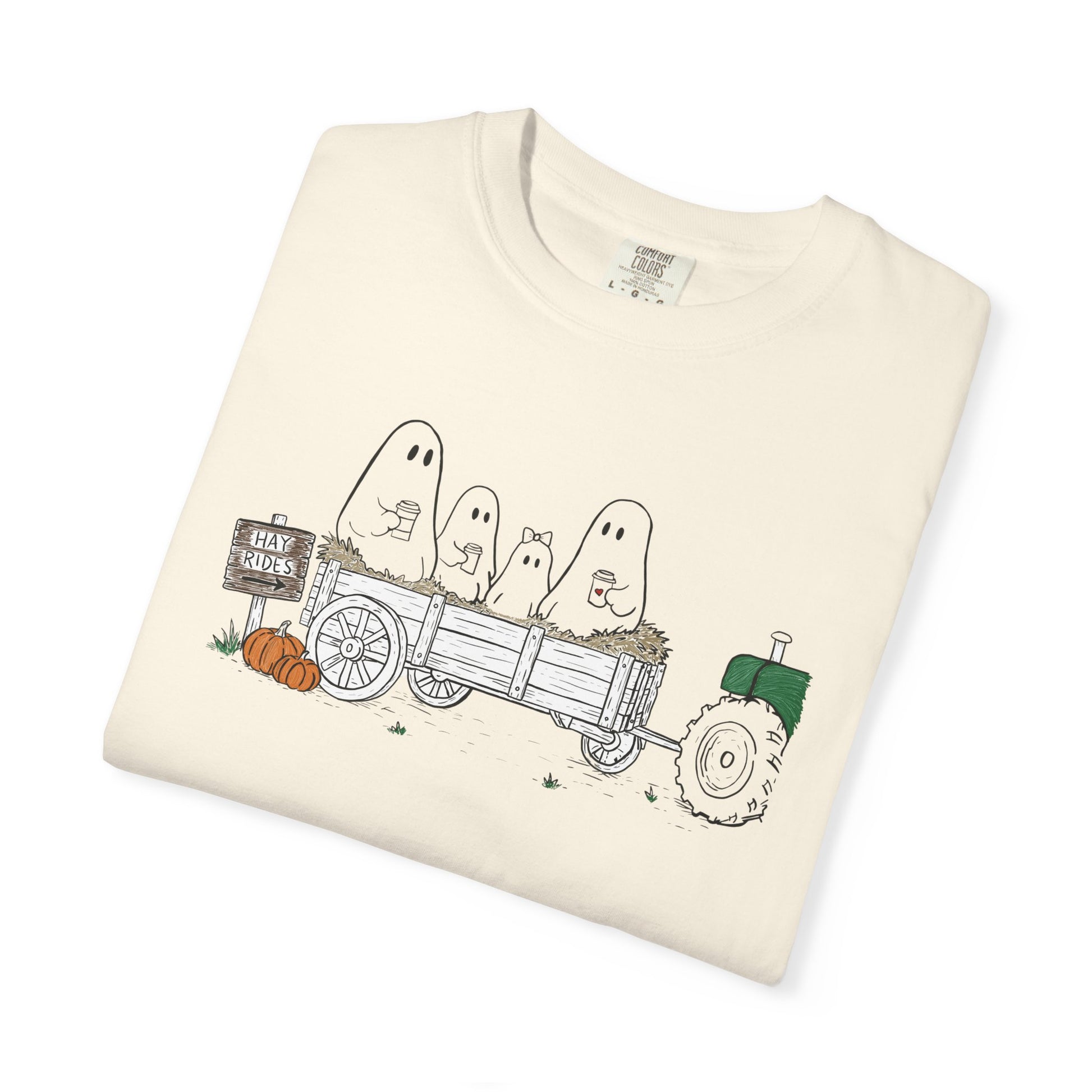 Comfort Colors ivory t-shirt featuring a hand-drawn ghost family riding in a hay wagon with pumpkins, coffee mugs, and a vintage tractor from The Story of the Ghost Chapter 1 collection.