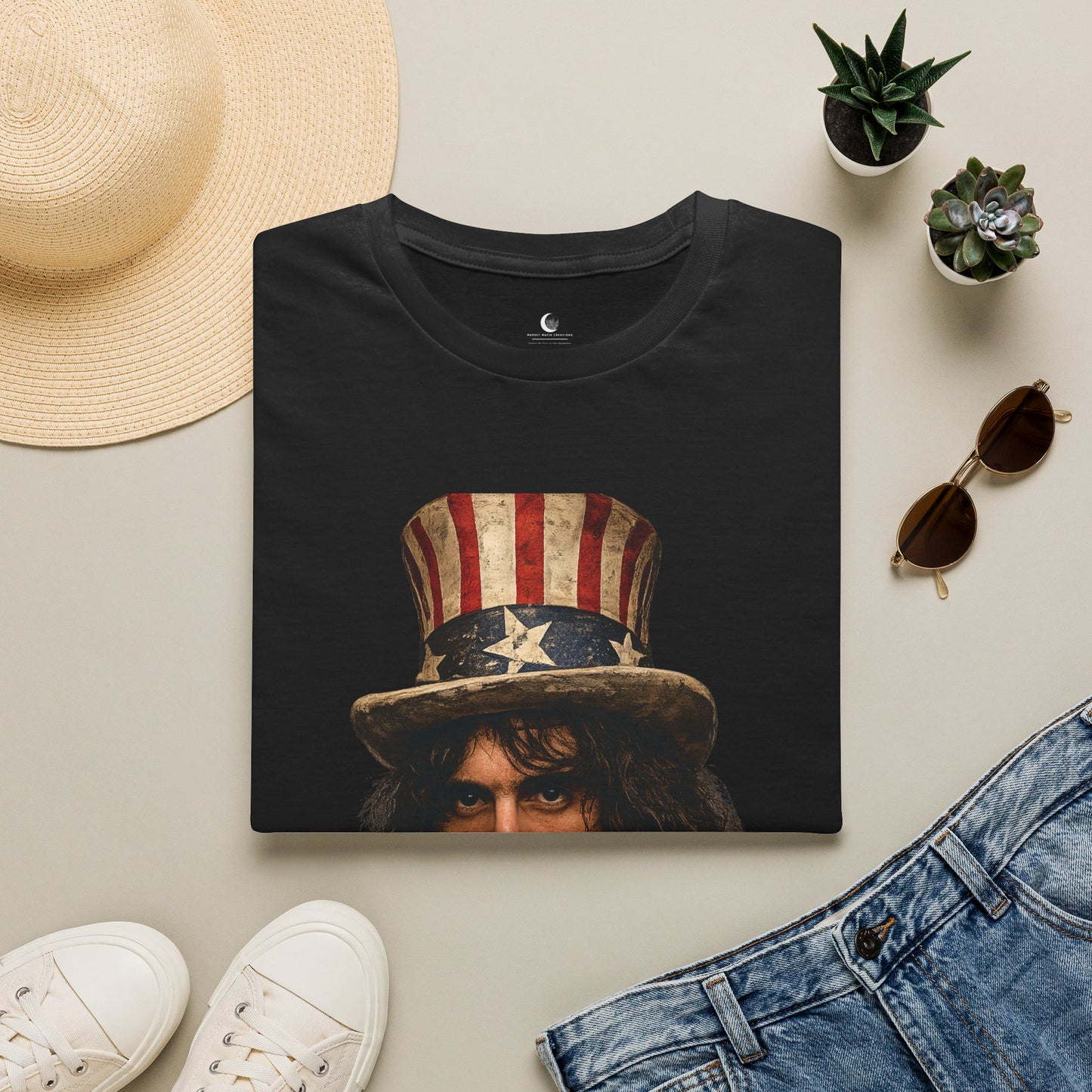Black t-shirt with graphic design of a person wearing an American flag hat, placed on a light surface with a hat, sunglasses, and jeans around it.