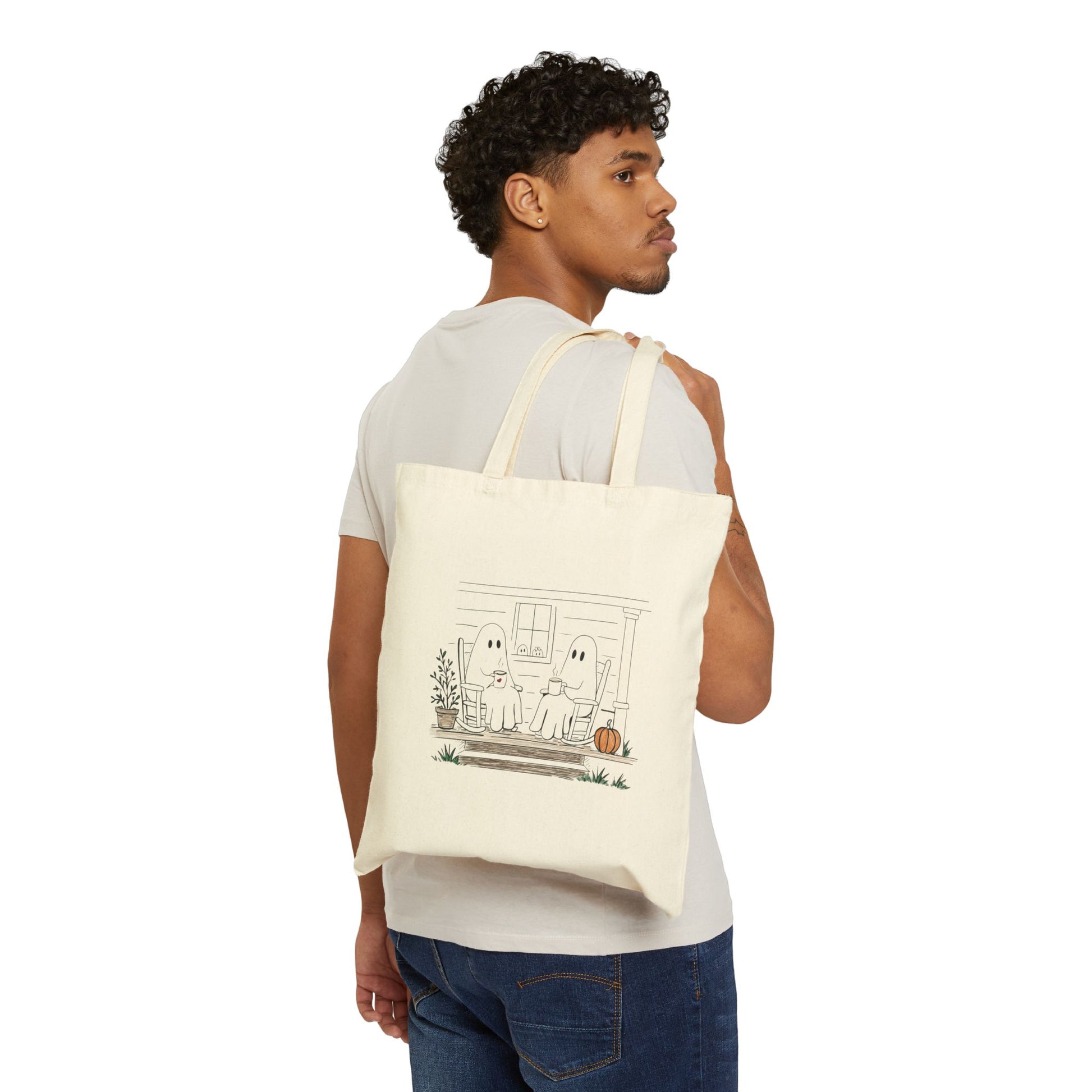 Natural canvas tote bag featuring a hand-drawn ghost family relaxing with coffee in rocking chairs on a front porch, with two little ghosts peeking through the window, a pumpkin, and subtle fall accents.