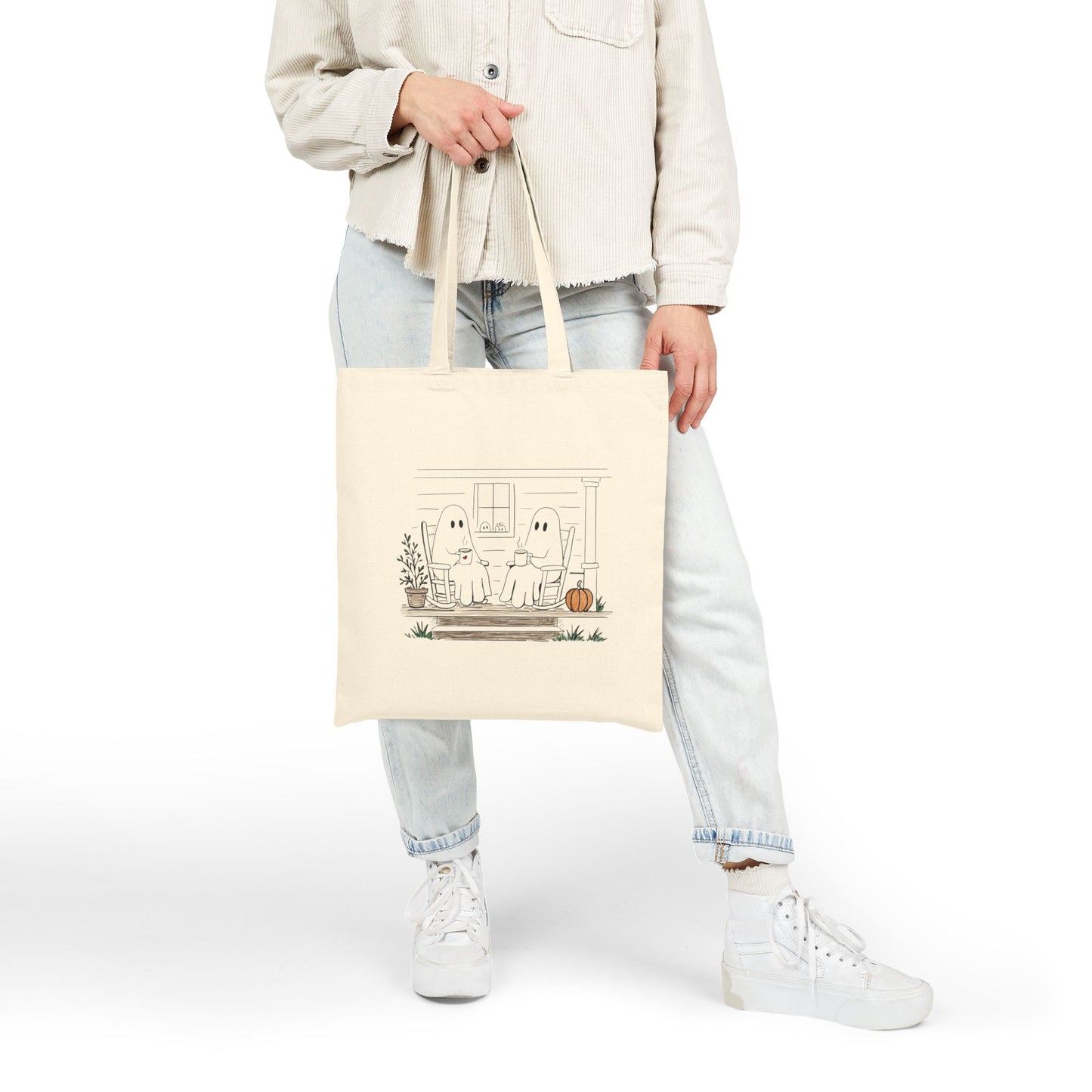 Natural canvas tote bag featuring a hand-drawn ghost family relaxing with coffee in rocking chairs on a front porch, with two little ghosts peeking through the window, a pumpkin, and subtle fall accents.