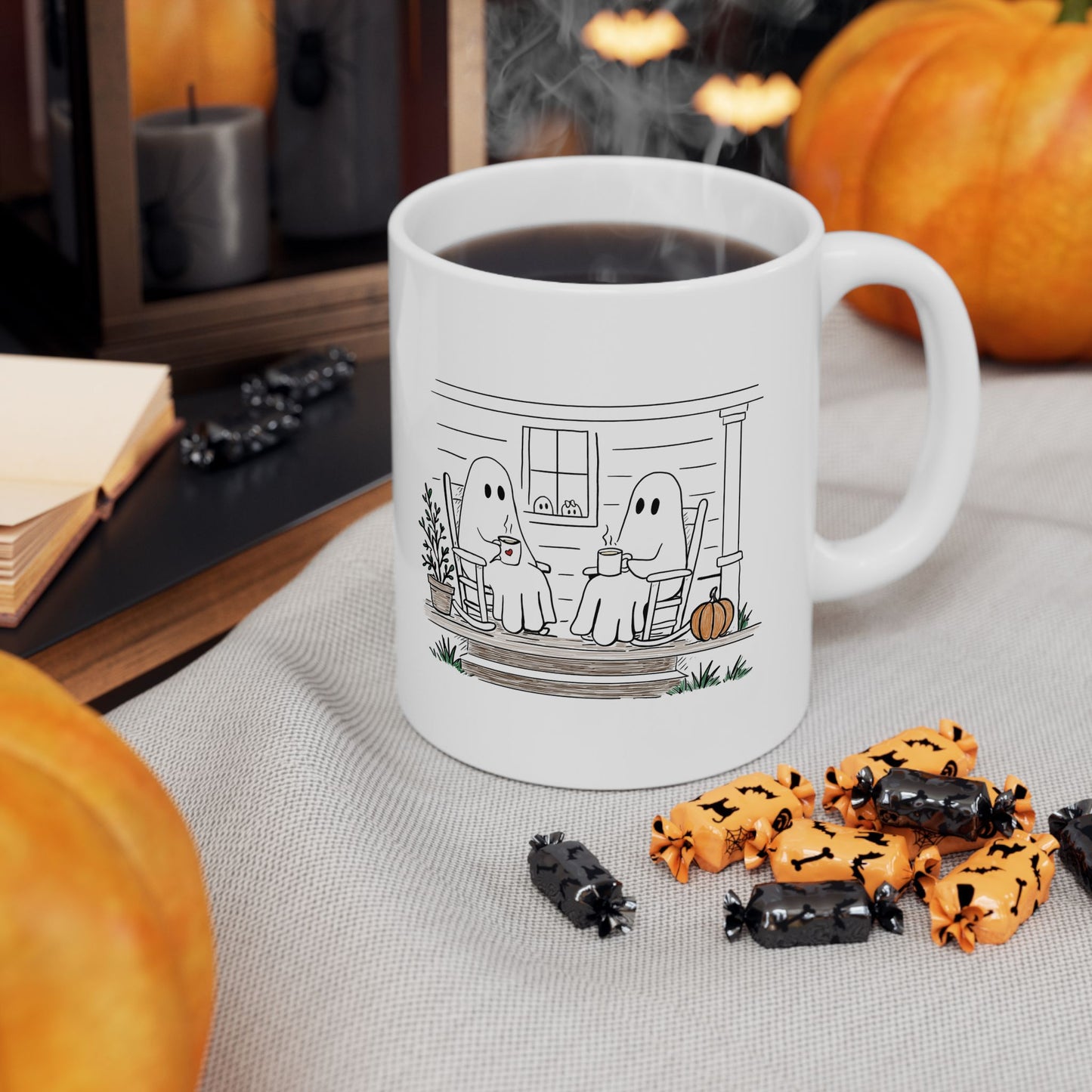 White ceramic mug featuring a hand-drawn ghost family sitting on a front porch in rocking chairs with coffee, with two little ghosts peeking through the window and subtle fall color accents.