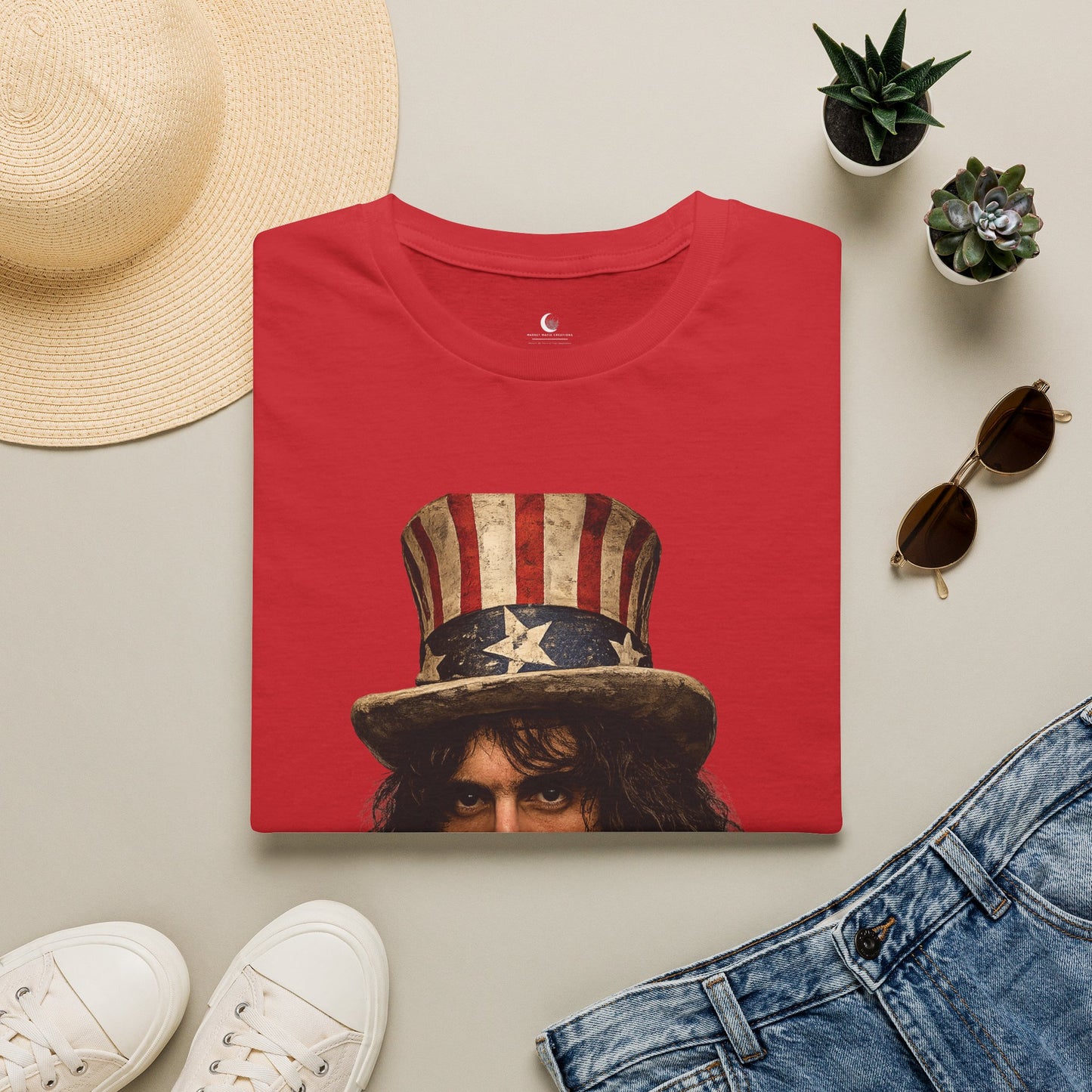 Red t-shirt with a graphic design of a person wearing an American flag hat, surrounded by a straw hat, sunglasses, white sneakers, and denim jeans on a light gray background.