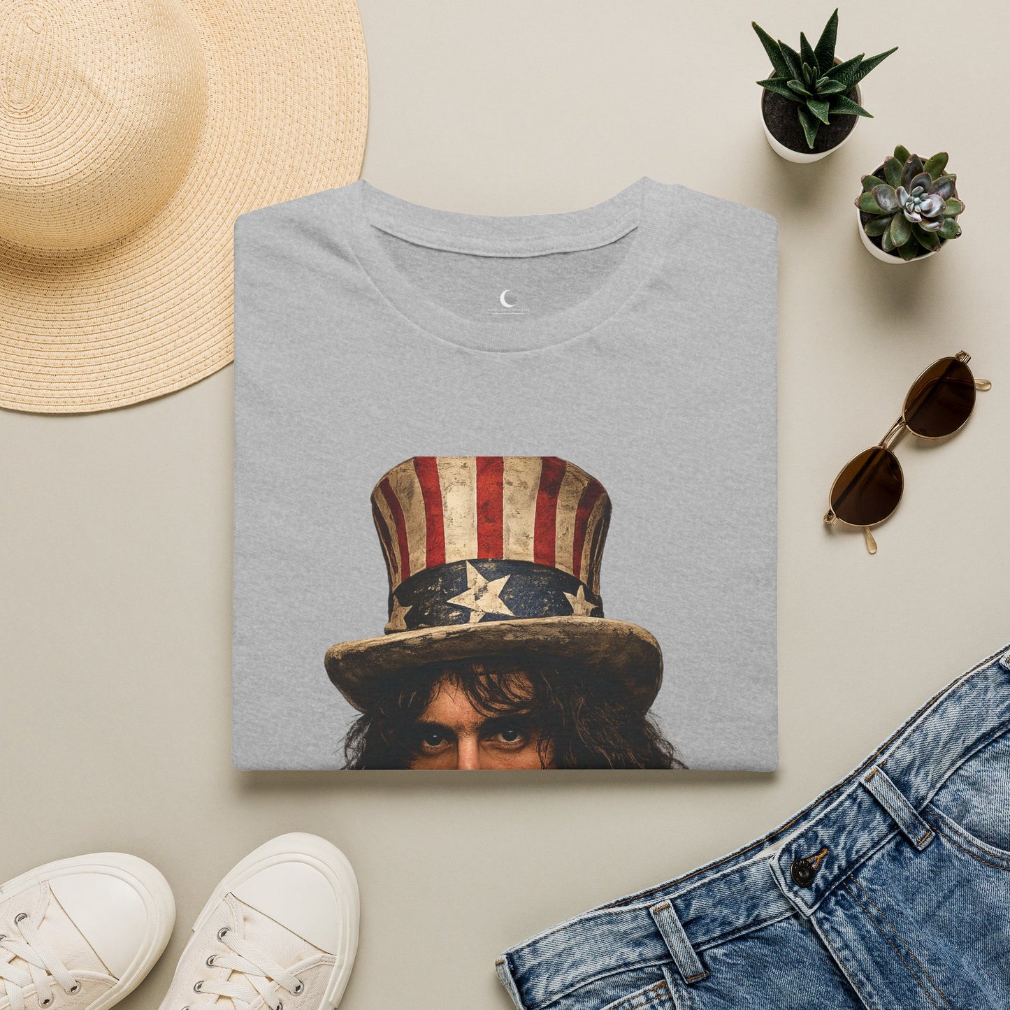 Gray t-shirt with graphic design of a person wearing an American flag hat, surrounded by a straw hat, sunglasses, white sneakers, and denim jeans on a light background.