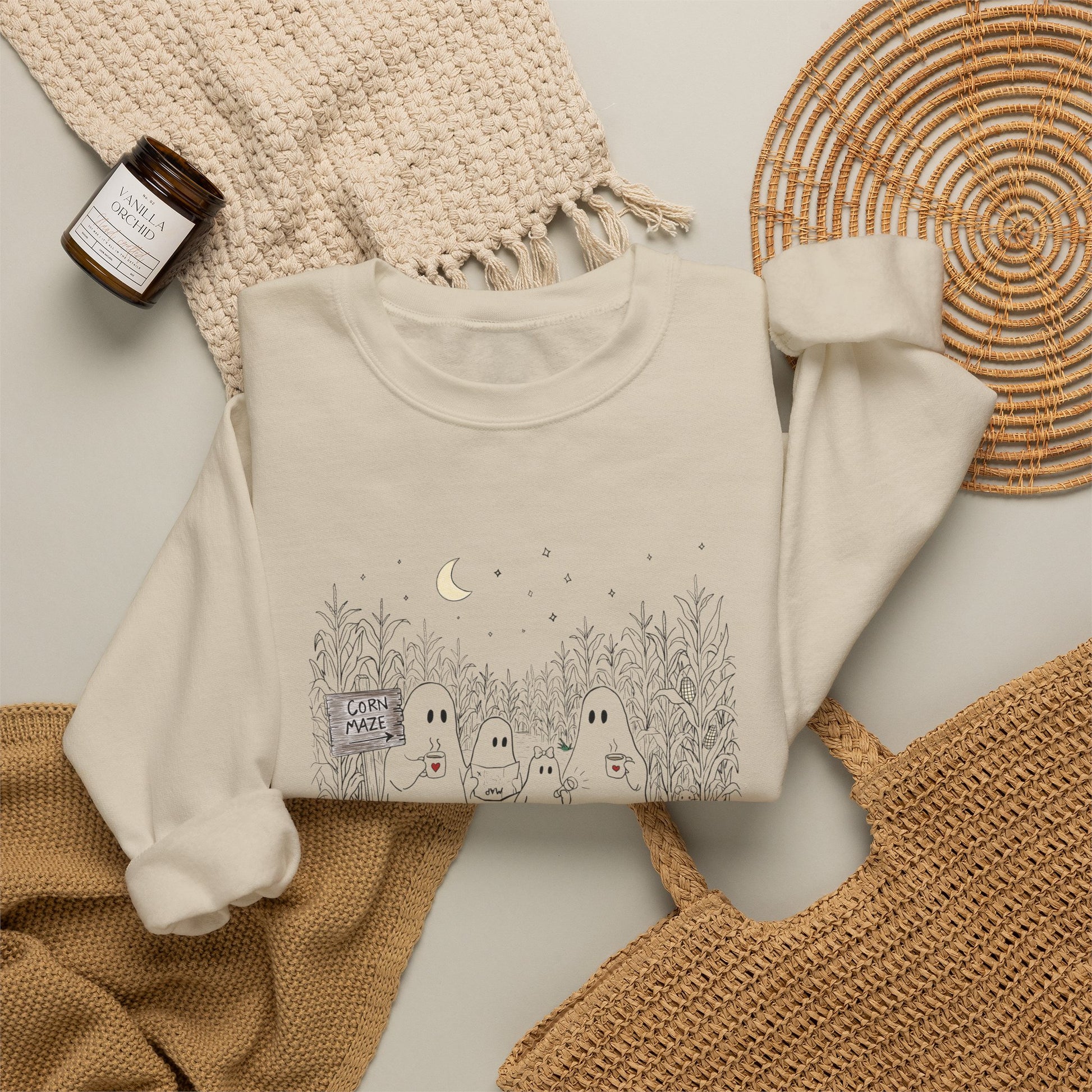 Crewneck sweatshirt featuring a hand-drawn ghost family walking through a moonlit corn maze with warm drinks, tall corn stalks, and a pumpkin from The Story of the Ghost Chapter 2 collection.