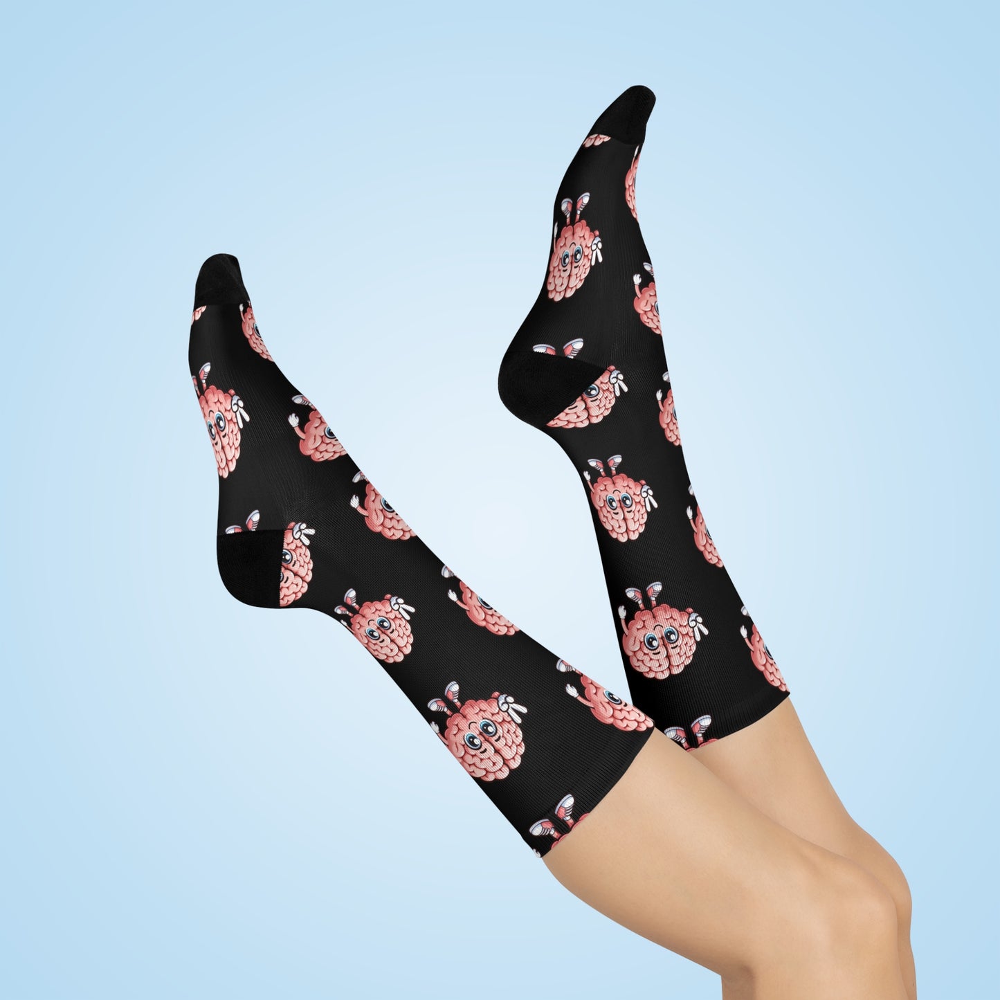 A pair of black crew socks with a pink and white cartoon brain pattern, shown on a model's legs against a light blue gradient background.