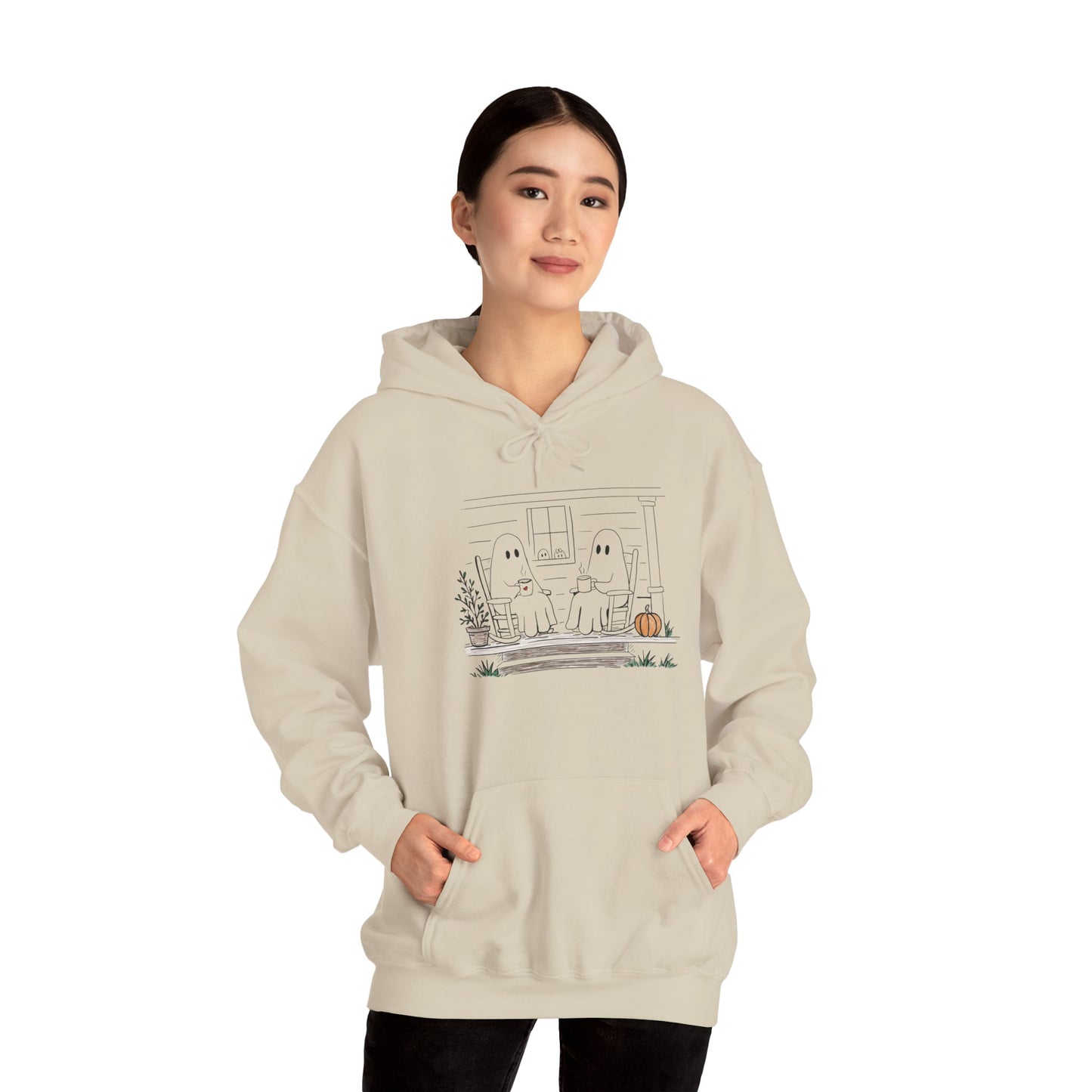 A woman modeling a light beige hoodie with a cute ghost graphic on the front, set against a plain white background.