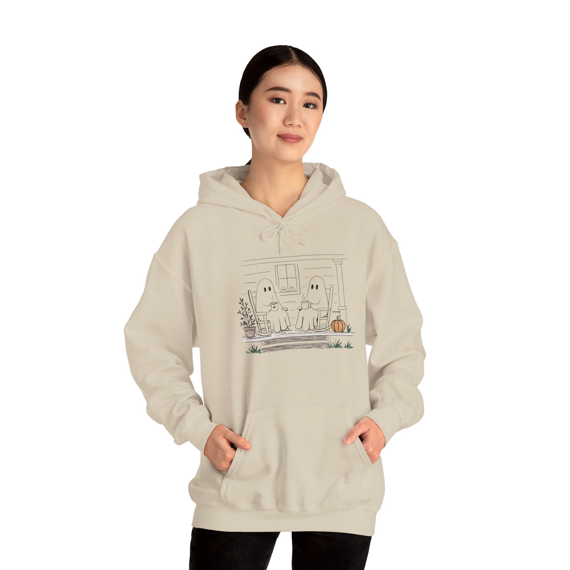 A woman modeling a light beige hoodie with a cute ghost graphic on the front, set against a plain white background.