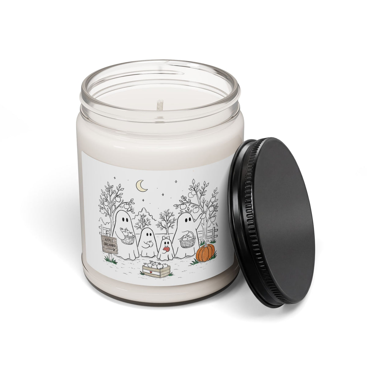 A white wax candle in a clear glass jar with a black metal screw-on lid leaning against it. The front label features a cute Halloween illustration of four white ghosts in a spooky yard with trees, a pumpkin, and a crescent moon.