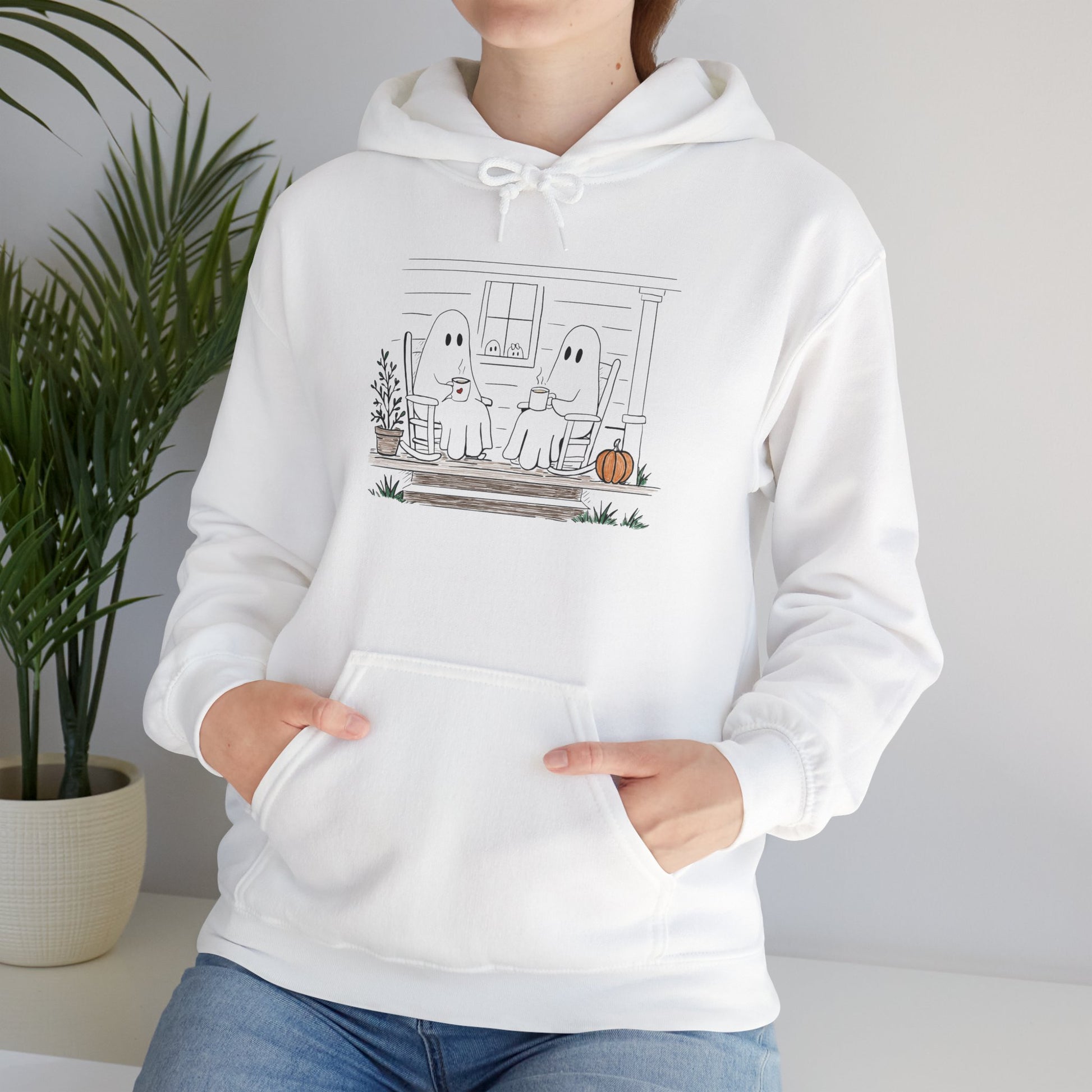 Pullover hoodie featuring a hand-drawn ghost family enjoying coffee in rocking chairs on a front porch, with two little ghosts peeking through the window, a pumpkin, and subtle fall color accents.