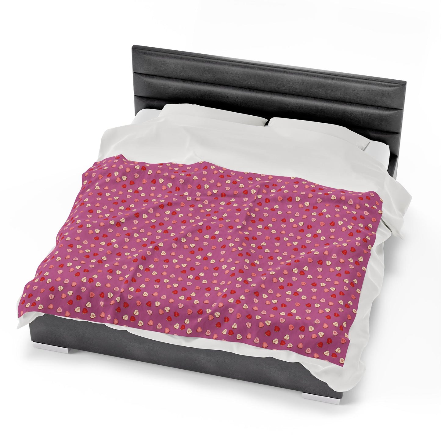 A plush blanket with a hand-drawn design of red candy hearts on a white background, placed on a black cushioned surface.