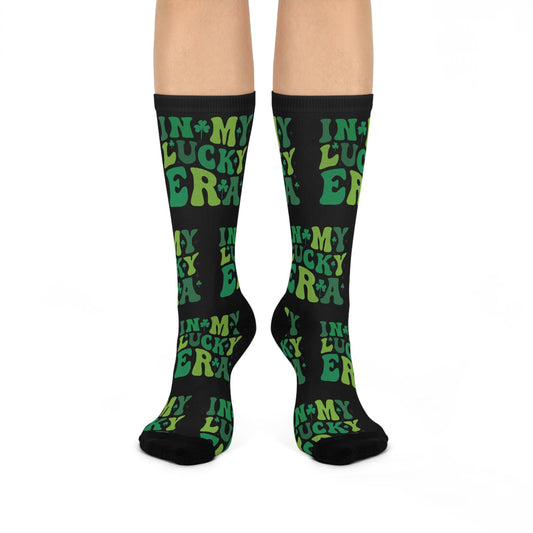 A pair of crew socks with a pattern of the phrase 'Lucky Irish' in a repeating design. The socks are black with green text and yellow accents.