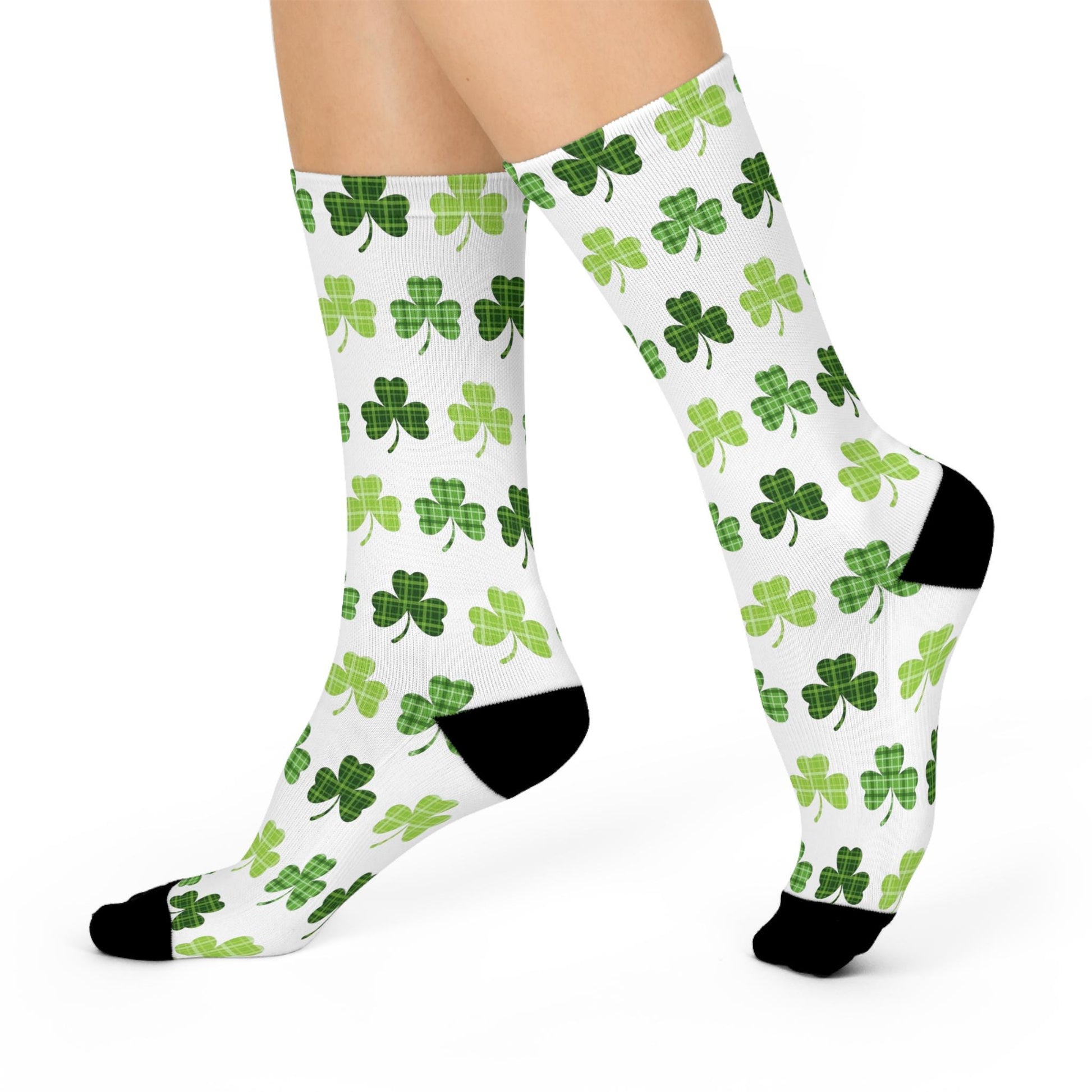 A pair of white crew socks with an all-over print of green clover leaves, worn on the feet.